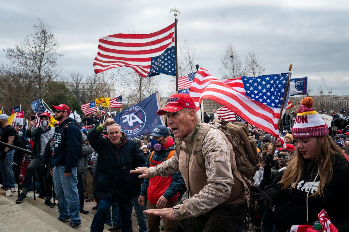 Ray Epps, in a red Trump hat, center, gestures to a line of law enforcement officers