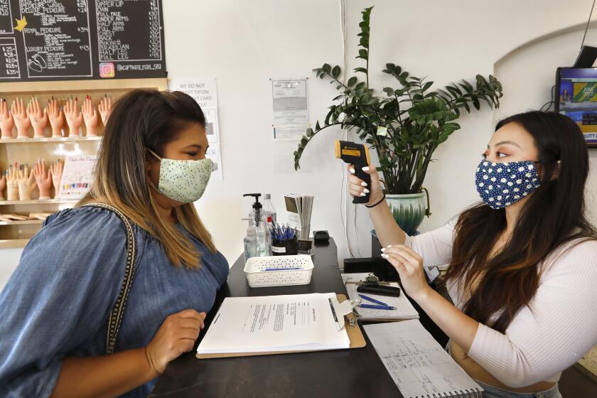 FULLERTON,CA-JUNE 19 2020--Melissa Alatorre, left, gets her temperature checked by Christina Dinh, right, and signs a release before getting her nails done at Captivate Nail & Spa, on the first day of reopening. Captivate Nail & Spa in Fullerton is one of the nearly 11,000 nail salons in the state. Crystal Trang Luong opened the salon only five months before the coronoavirus threat caused her to shut down. After nearly three months closure, June 19, 2020 marks the first day nail salons can reopen under state law. (Carolyn Cole/Los Angeles Times)