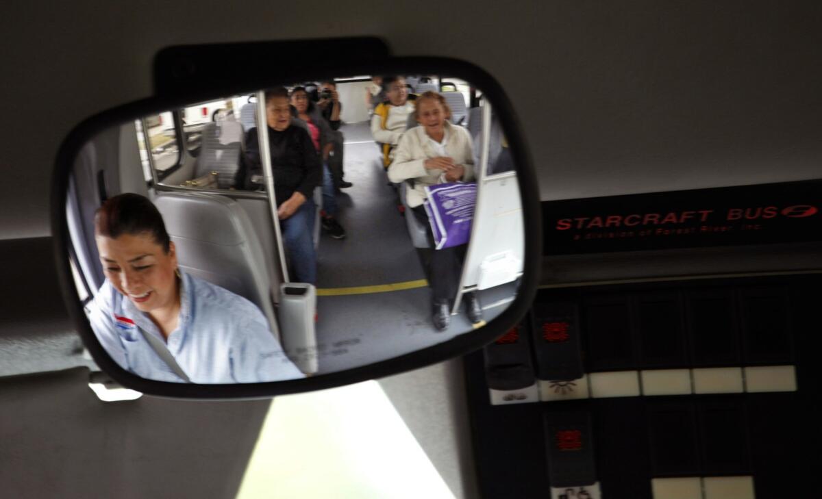 Dial-A-Ride bus driver Laura Torres, reflected in the mirror at left, shares a light moment with her passengers. She greets each rider in a loud, playful voice: "Come in, come in. Where are we going today?" Half the time, she doesn't need to ask. She knows nearly everyone's address by heart.