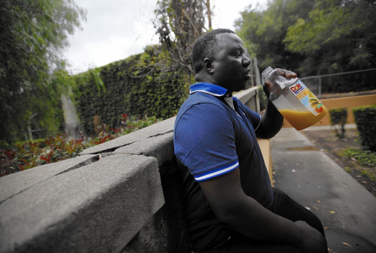 Musa Kalawa drinks juice on a walkway at the St. Andrews Garden apartments across the wall from the Freeport-McMoRan Oil and Gas drilling site in South L.A. Residents are concerned about oil fumes and possible expansion at the business.