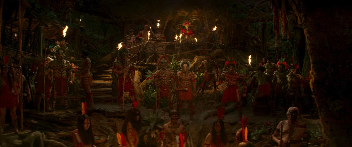 People in tribal garb dance in a line surrounded by fire torches