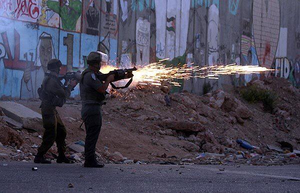An Israeli soldier shoots tear gas toward Palestinian protesters, not visible, in the West Bank refugee camp of Kalandia, north of Jerusalem.