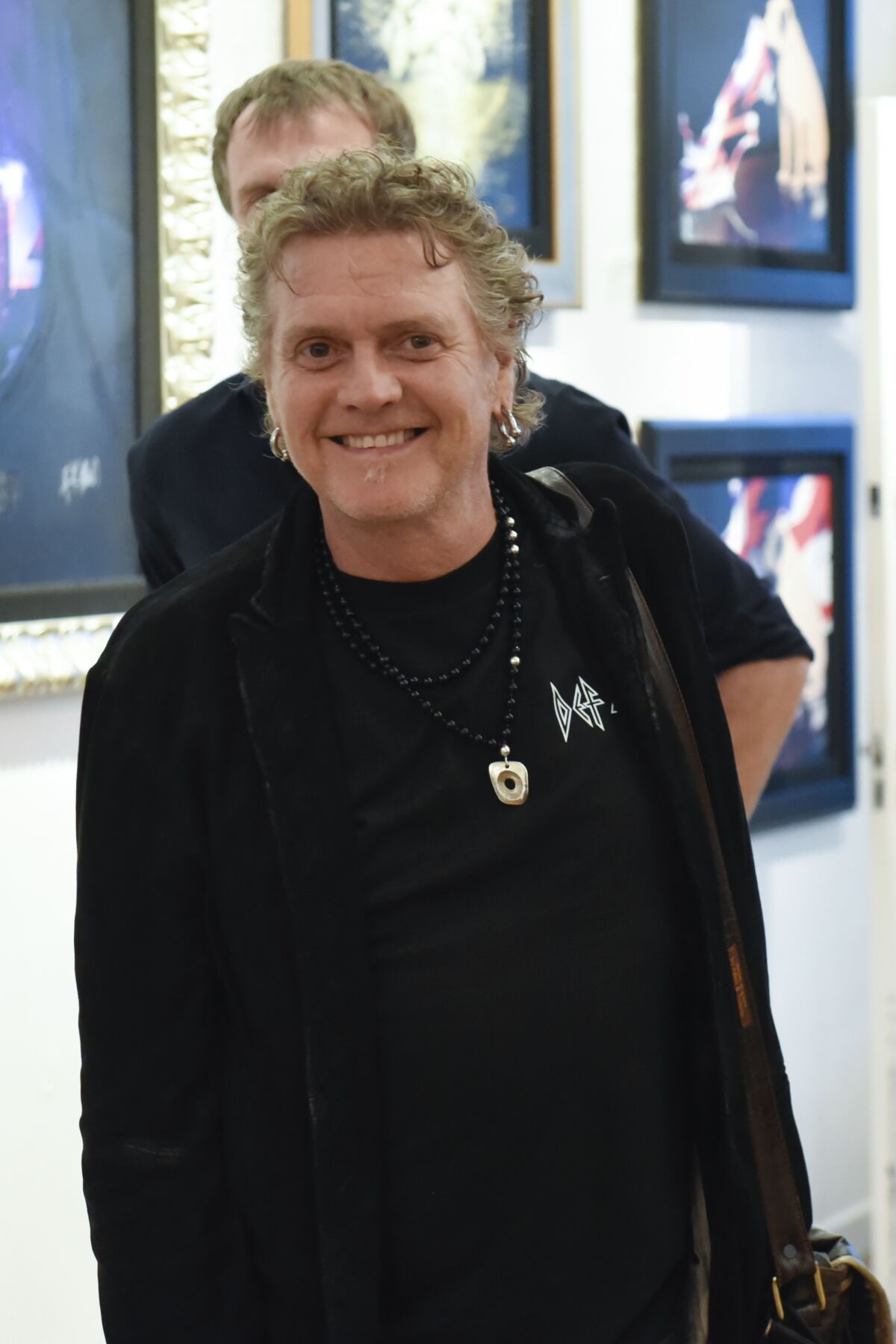 A man with short and curly gray hair wearing a black shirt and jacket and smiling
