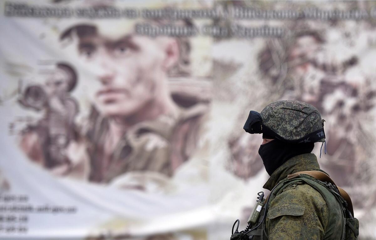 A Russian soldier stands in front of a recruitment poster for the Ukrainian armed forces Thursday near a surrounded Ukrainian military unit in the Crimean town of Perevalnoye.