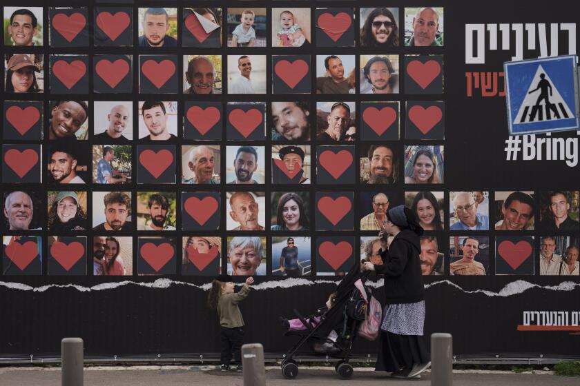ARCHIVO - Una mujer y sus hijos pasan junto a un muro con fotografías de rehenes secuestrados durante el ataque transfronterizo de Hamás en Israel el 7 de octubre de 2023, el 26 de febrero de 2024, en Jerusalén. (AP Foto/Leo Correa, Archivo)