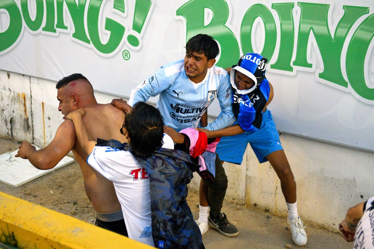 Three people at a soccer game appear to attack a fourth, who is not wearing a shirt