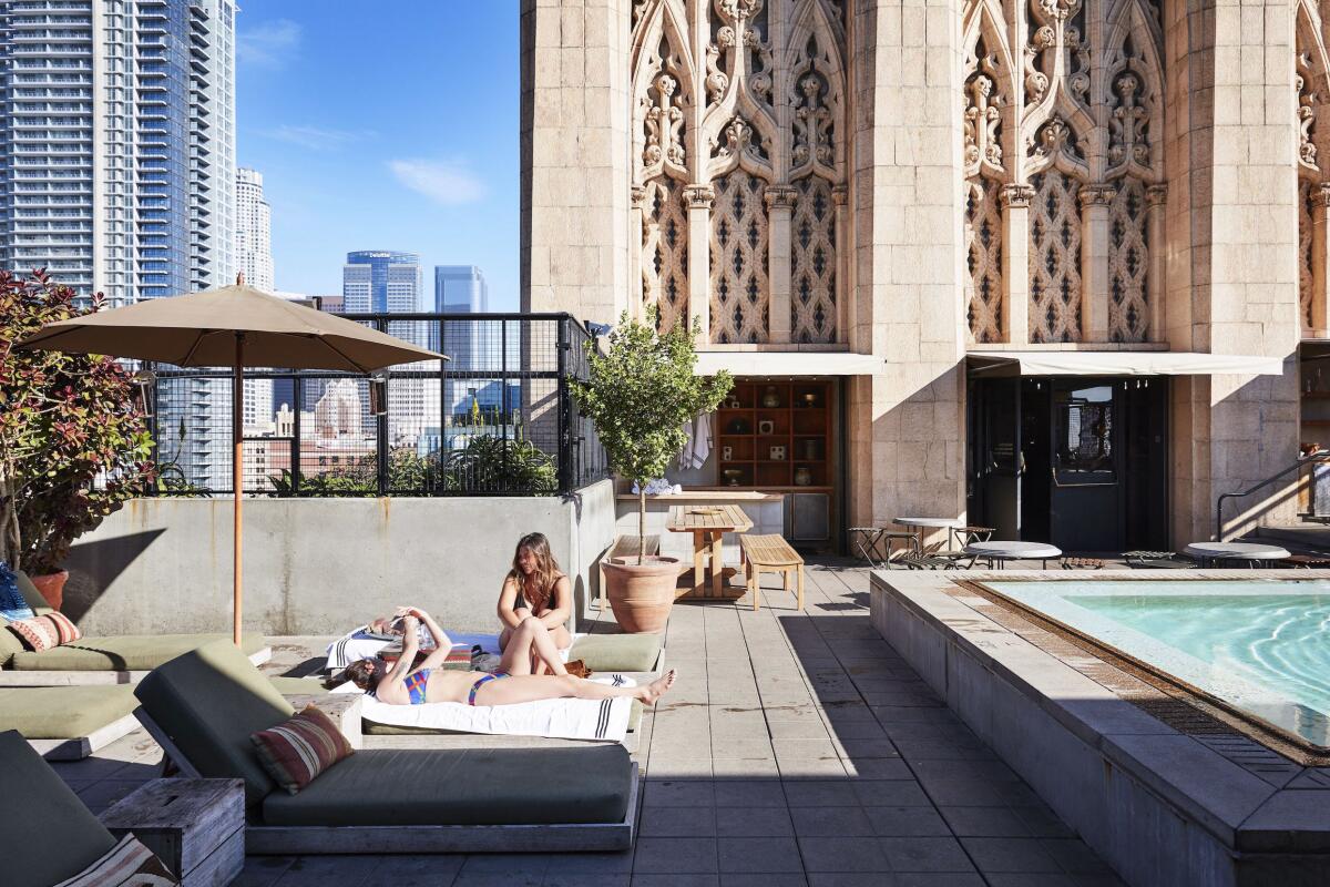 a rooftop with lounge chairs and a pool with tall buildings in the background