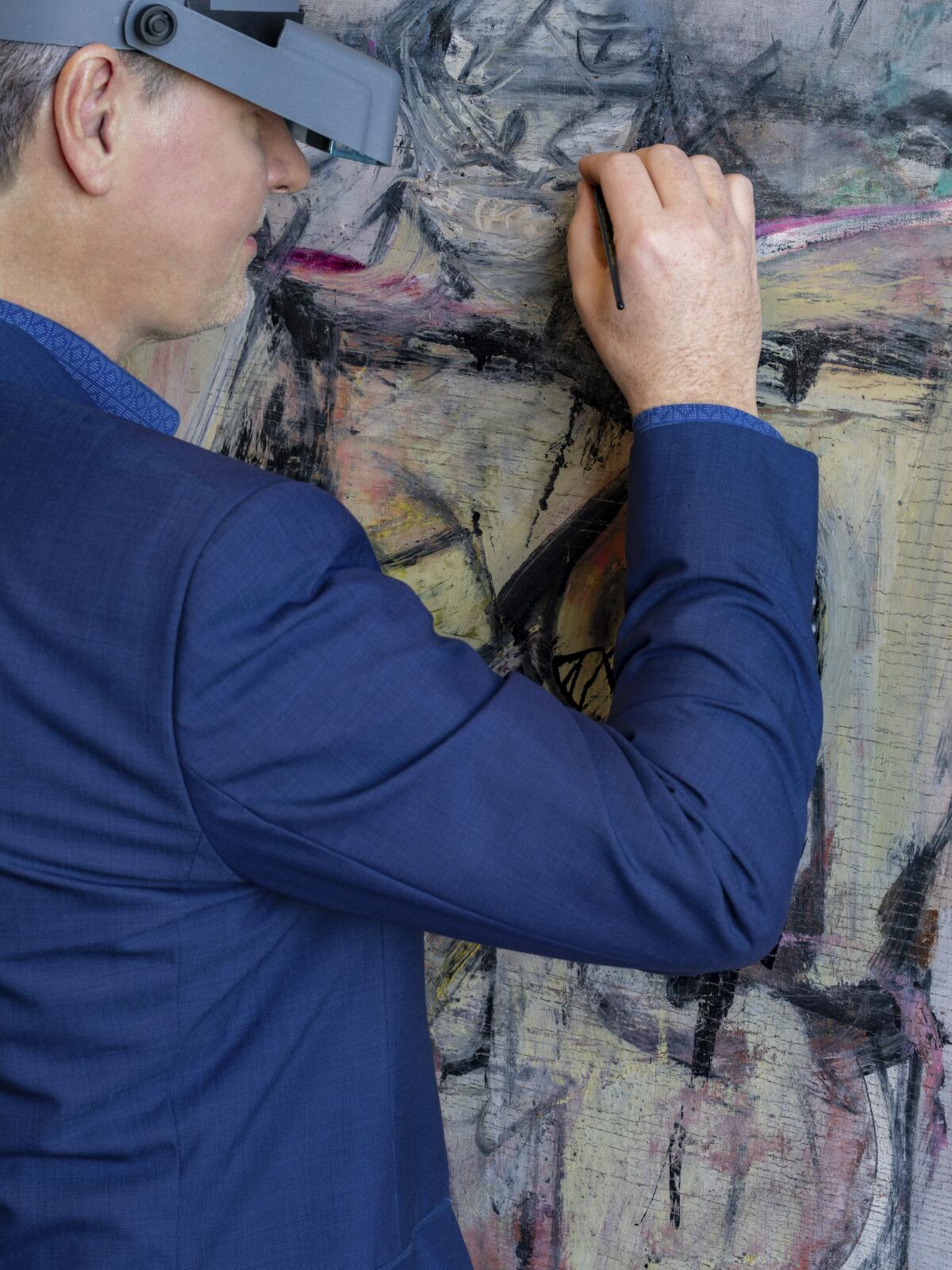 A man uses special headgear for magnification delicately uses a brush on a painting. 