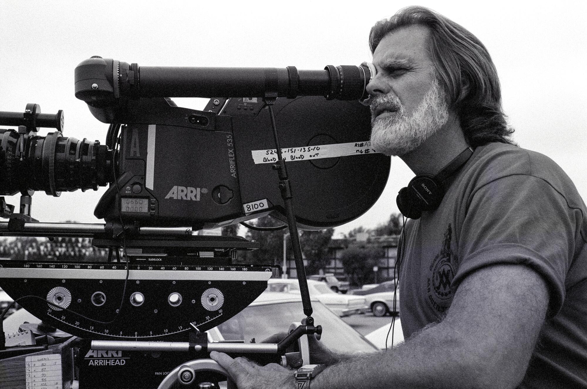 Director Taylor Hackford looks into the viewfinder of a film camera.