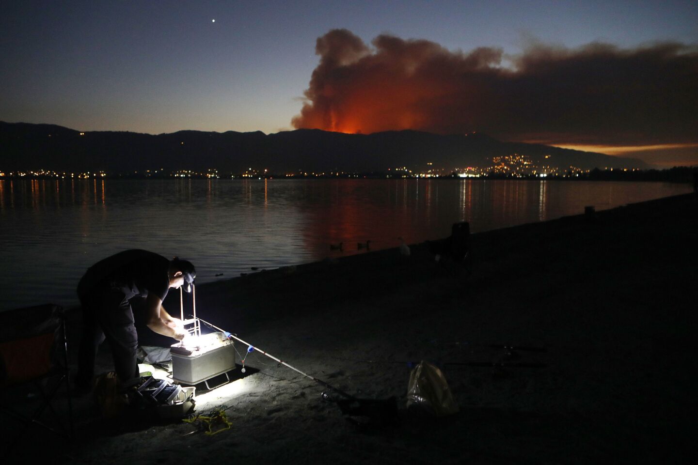 A man prepares to fish as smoke rises from the Holy fire in the Cleveland National Forest in Lake Elsinore on Aug. 6.