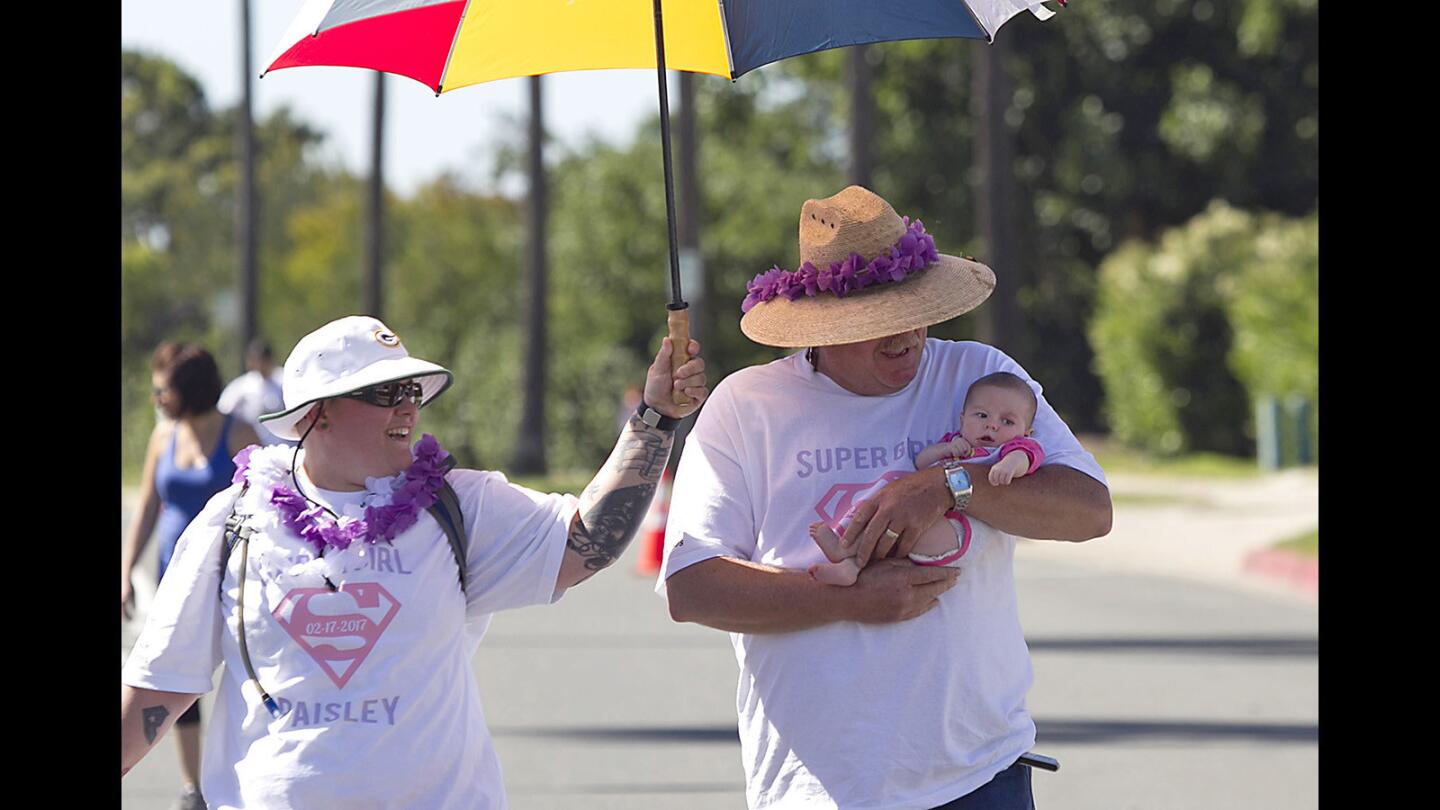 Jen Caballero, left, holds a shade umbrella for Don Willman and his granddaughter Paisley as they walk in the Orange County March for Babies, part of the March of Dimes at Fashion Island in Newport Beach on Sunday. The March of Dimes promotes children’s health by working to prevent birth defects and other conditions.