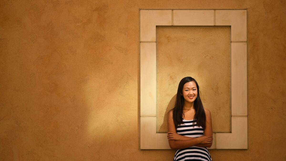 Katherine Ho leans against a wall, arms crossed, as she poses for a photo.