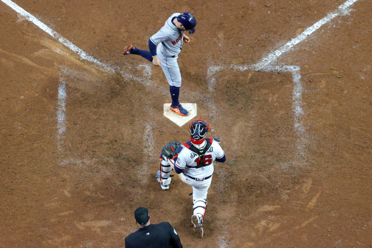 A baseball player touches home plate as the catcher kneels behind it.