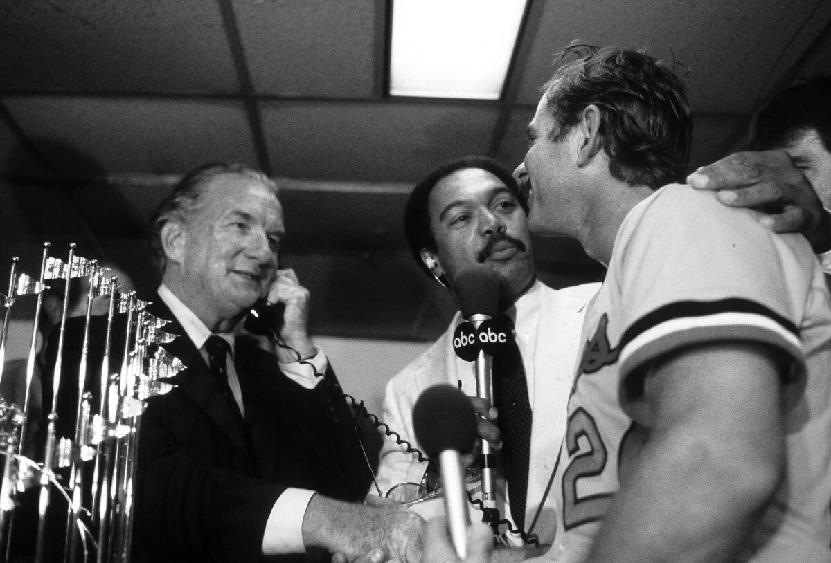 The Orioles' Rick Dempsey shakes hands with team owner Edward Bennett Williams as Reggie Jackson does an interview for ABC after Baltimore won the 1983 World Series.