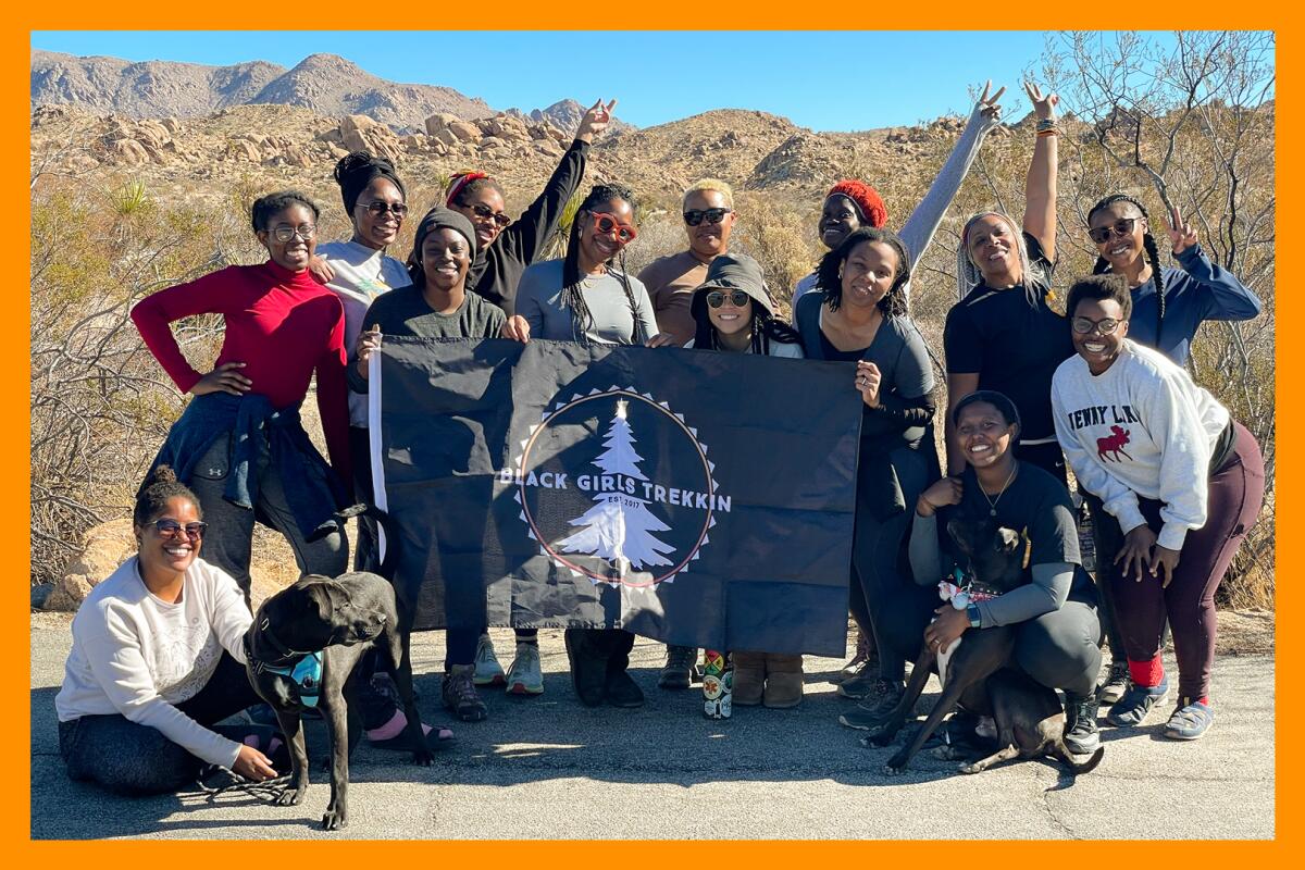 A group of hikers (and a couple dogs) stand and crouch near a flag that says "Black Girls Trekkin'.