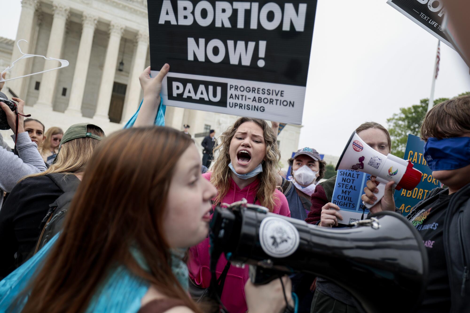 A young woman with a bullhorn faces a crowd. Her sign reads, "Progressive anti-abortion uprising."