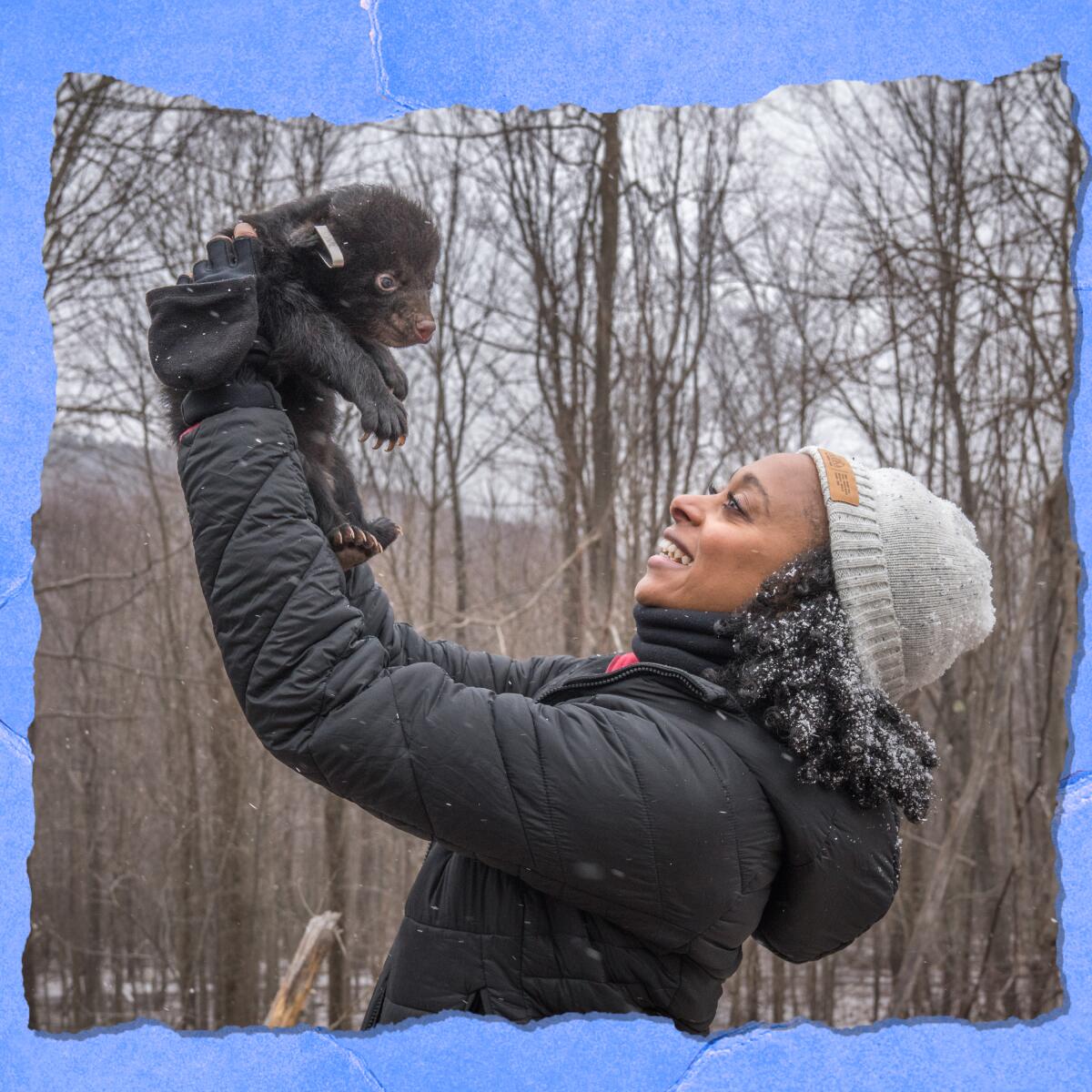 A smiling woman in a knit cap and a coat holds a baby bear.