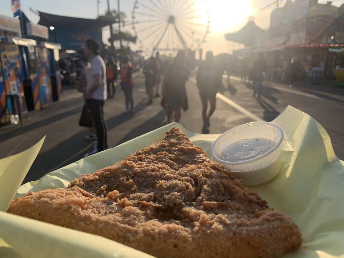 A slice of fried pizza with a Ferris wheel and a crowd in the background