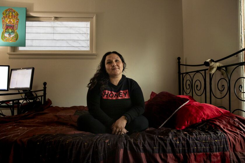 San Diego, California - December 07: Julie Corrales sits on her bed for a portrait after the Barrio Logan Community Plan update was approved by city council in Barrio Logan on Tuesday, Dec. 7, 2021 in San Diego, California. Corrales works for the Environmental Health Coalition as a policy advocate that represents Barrio Logan. After the plan was approved she screamed in joy for her community. Corrales has spend the last few years trying to get the plan approved with one of the goals being to separate industry from neighborhood. "I remember the first time I came here… And I looked around and I was everywhere," she said. I was on the walls, I was in the art, I was in the language. And I'd never felt more at home." (Ana Ramirez / The San Diego Union-Tribune)