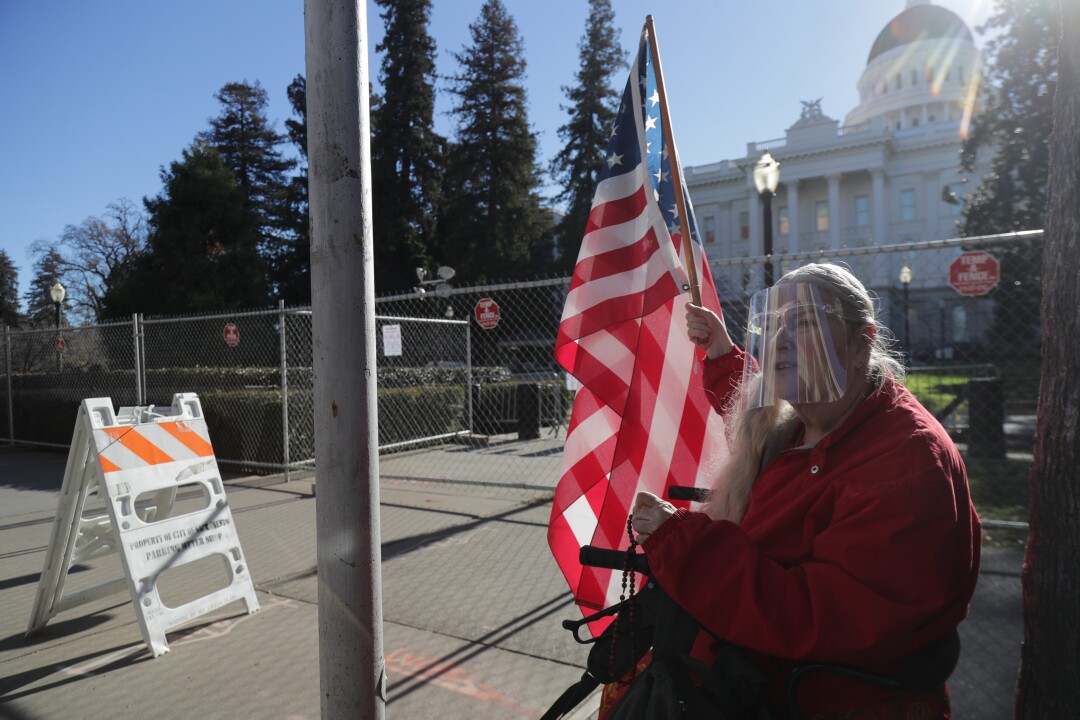 France Driscoll holding an American flag and rosary in front of state Capitol in Sacramento Saturday.