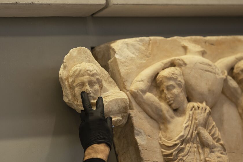 An Acropolis Museum staff places a male head on the frieze of the Acropolis museum during a ceremony for the repatriation of three sculpture fragments, in Athens, on Friday, March 24, 2023. Greece received three fragments from the ancient Parthenon temple that had been kept at Vatican museums for two centuries. Culture Ministry officials said the act provided a boost for its campaign for the return of the Parthenon Marbles from the British Museum in London. (AP Photo/Petros Giannakouris)