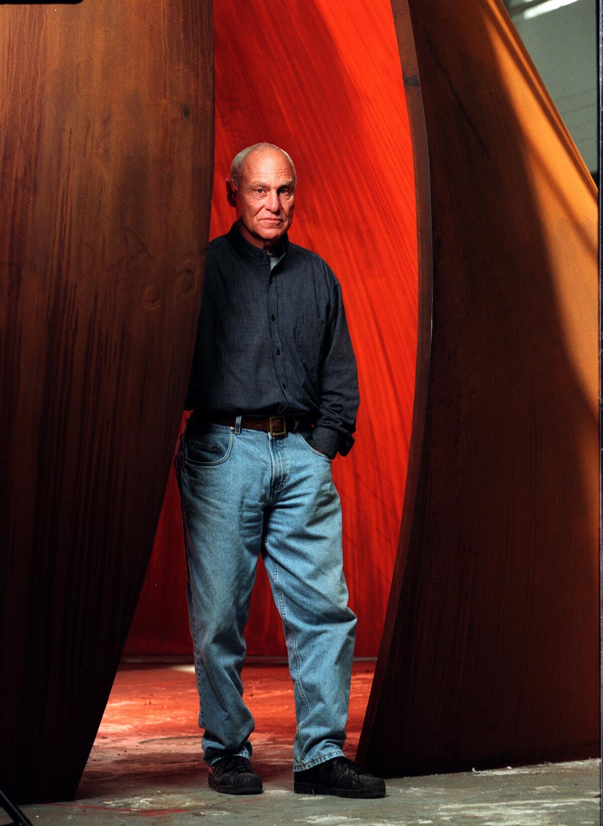 Sculptor Richard Serra, in jeans and a collared shirt, stands in a steel sculpture.