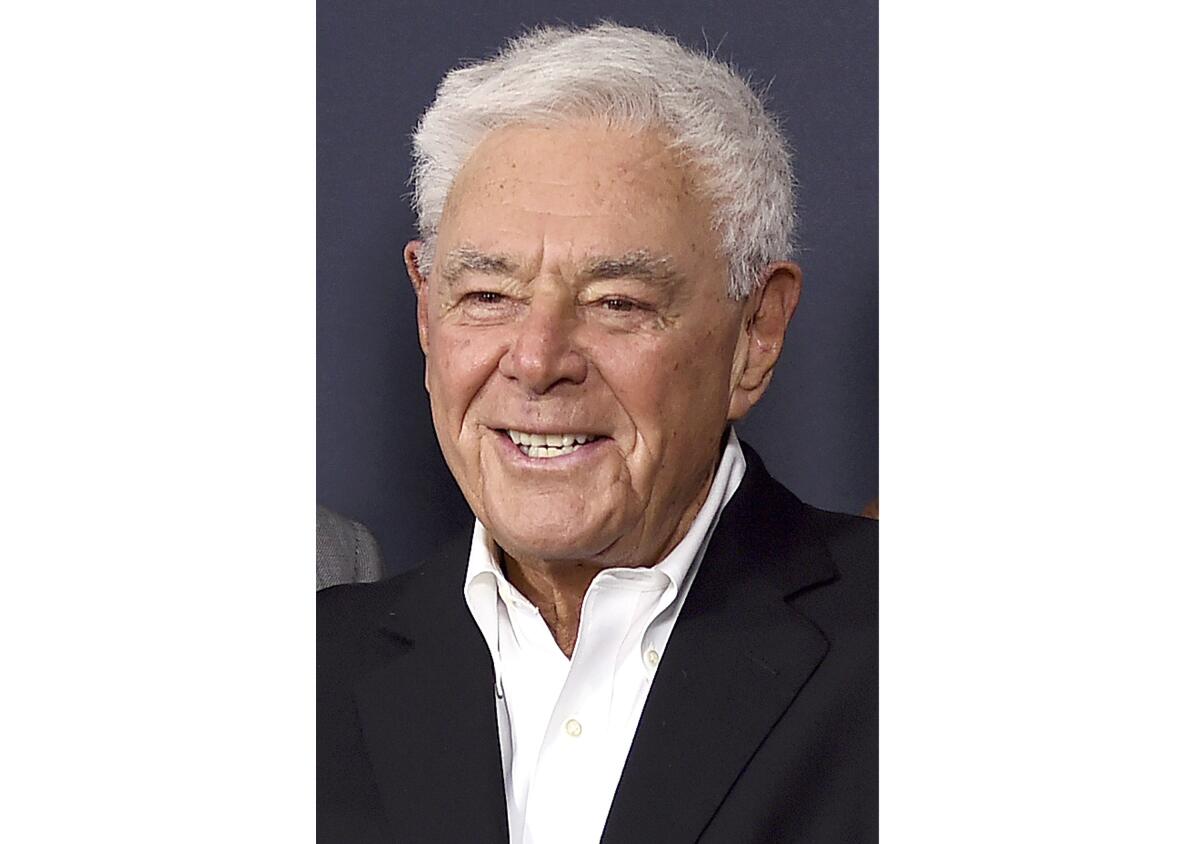 A headshot of a man with white hair wearing a white shirt and black sports coat