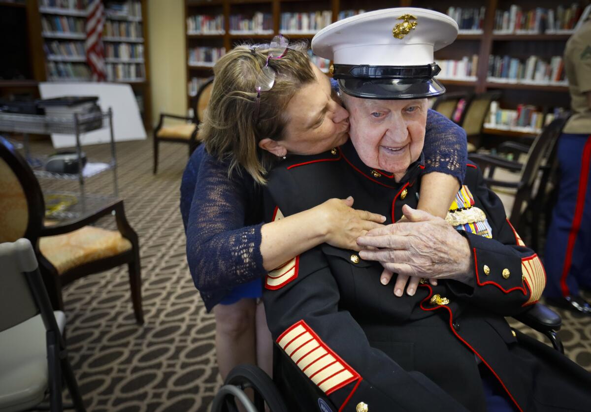 Retired U.S. Marine Corps First Sergeant John Farritor, wearing his dress uniform, is a veteran of some of the biggest battles of World War II in the Pacific and the Korean War, gets a hug and a kiss from his friend Kathryn Turner, during a party celebrating his 100th birthday, at Pacifica Senior Living, July 9, 2019, in Vista, California, where he lives.