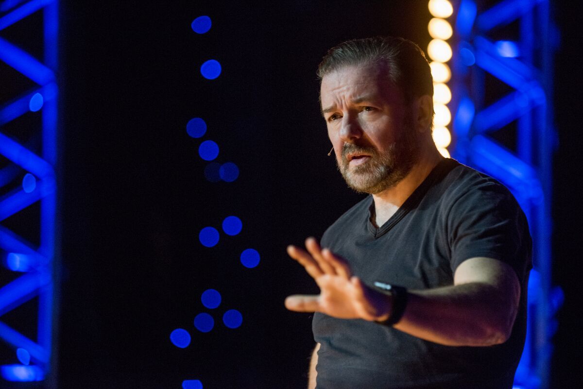 A man gestures on stage while wearing a microphone