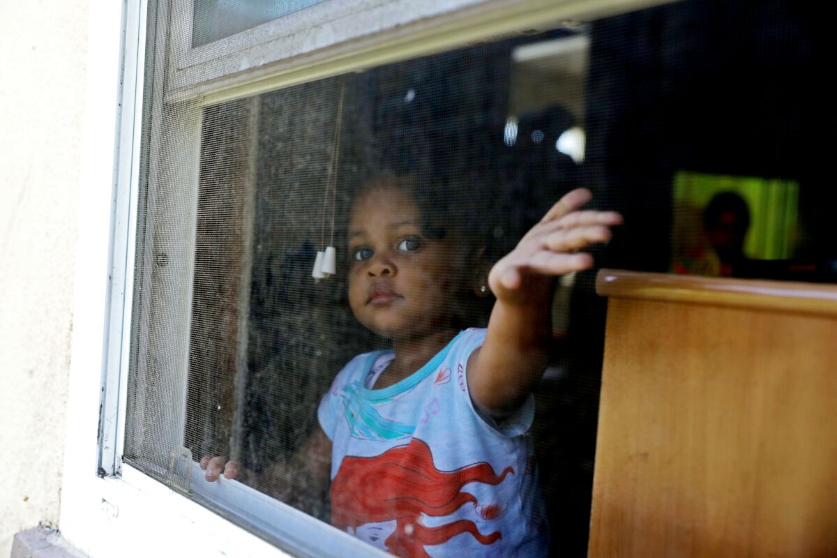 A young child holds her hand out a window