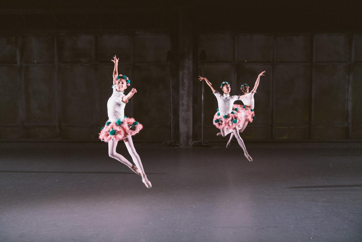 Three dancers in flowered tutus are seen mid-leap.