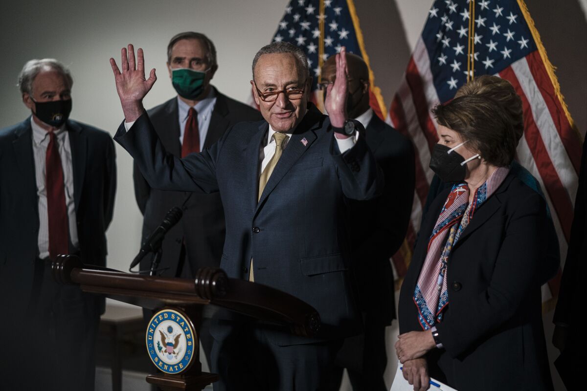 Senate Majority Leader Charles E. Schumer (D-N.Y.), flanked by other lawmakers, gestures as he speaks from a lectern.
