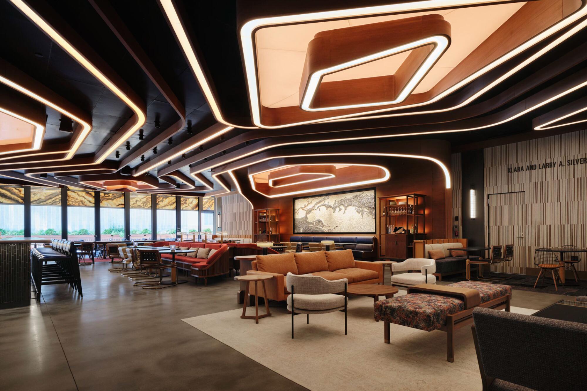 A restaurant sheathed in wood and warm earth tones features a geometric elements on the ceiling bordered with lighting.