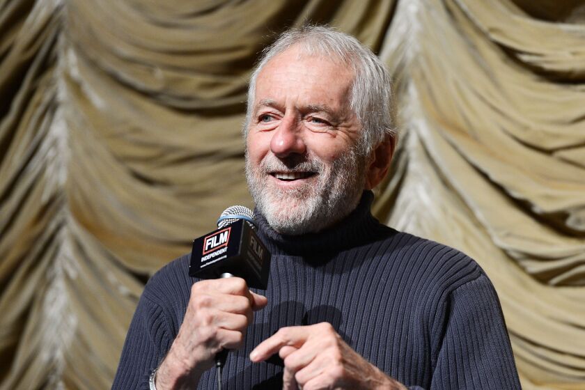 Barry Newman in a black turtleneck holding a microphone in his right hand and smiling