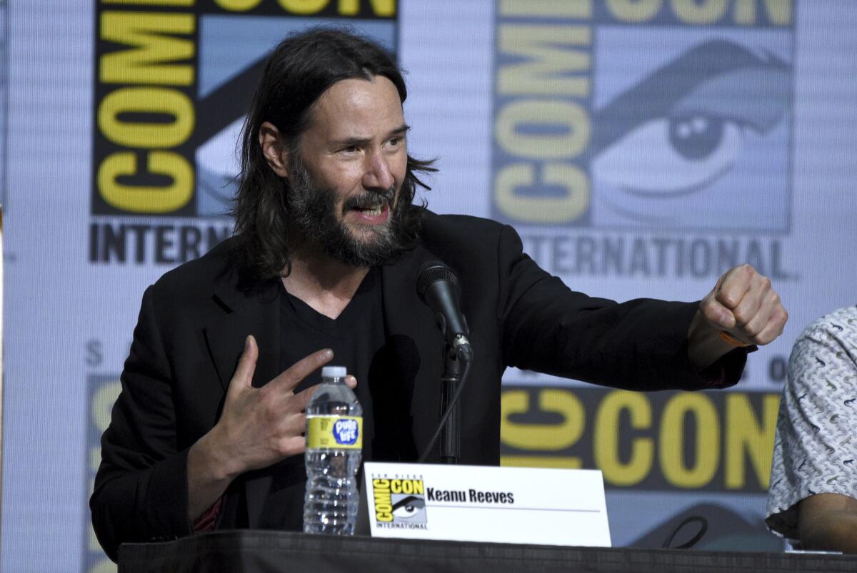 Keanu Reeves at a table with a Comic-Con banner behind him