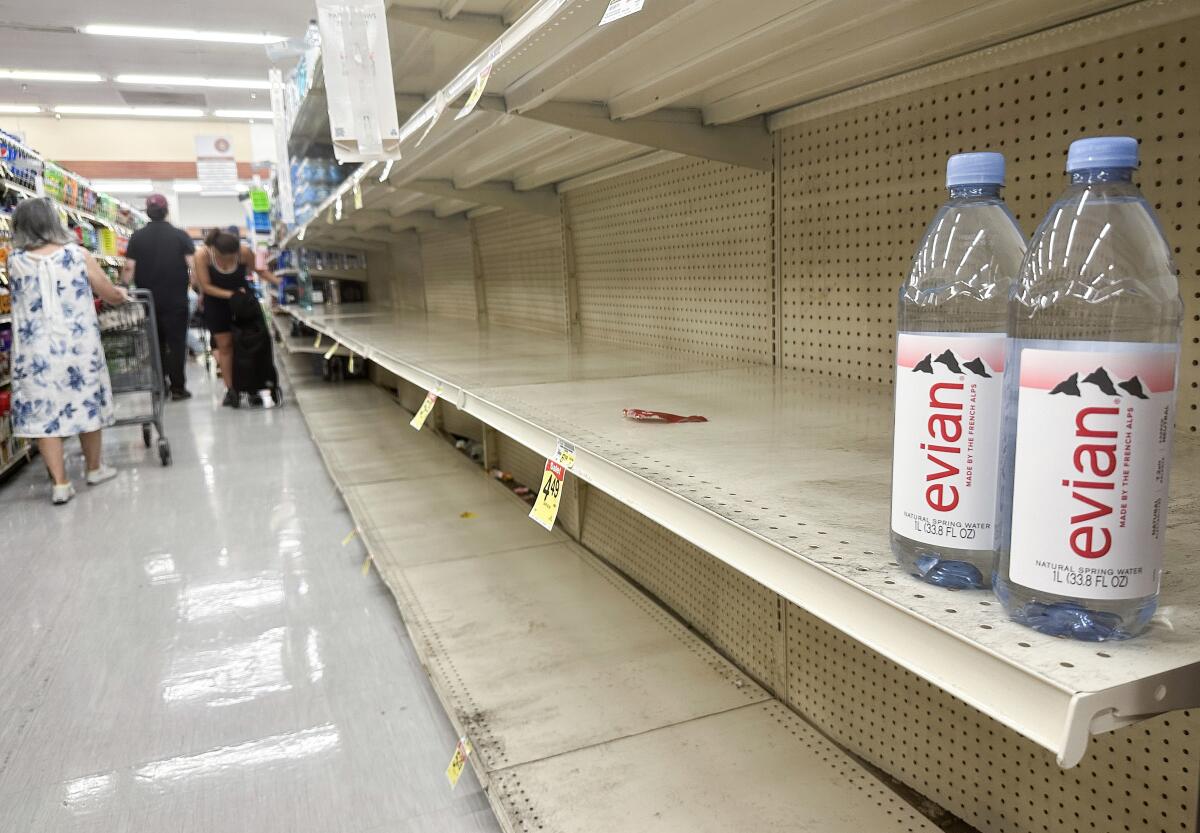 Two Evian bottles sit alone on an empty store shelf.