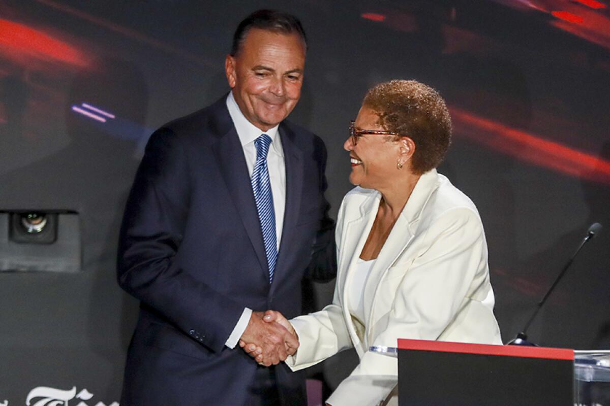 A man in a suit and tie and woman in a pantsuit smile and shake hands on a stage.