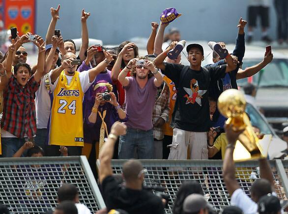 Fans standing on a bus stop kiosk scream out as the Lakers and Kobe Bryant pass by with the Larry O'Brien trophy during Monday's victory parade.