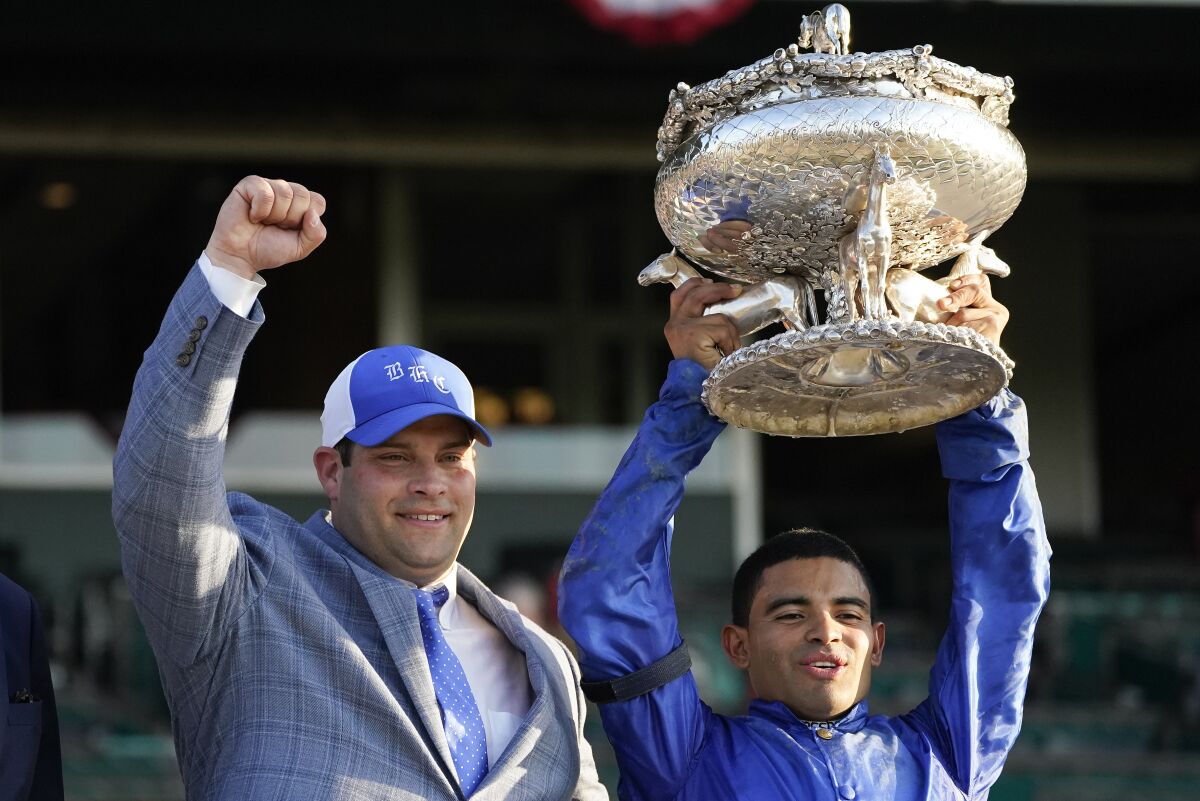 Trainer Brad Cox, left, and jockey Luis Saez celebrate with the August Belmont Trophy after Essential Quality's win.