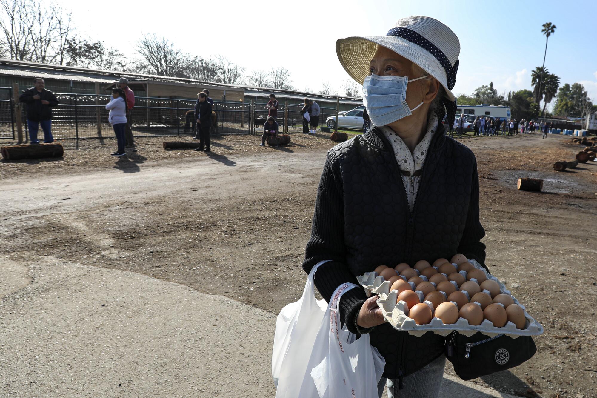 Xiao Ping, holding a tray of eggs, looks back at the long line of egg buyers in Chino. People started lining up early at Maust's California Poultry in Chino.