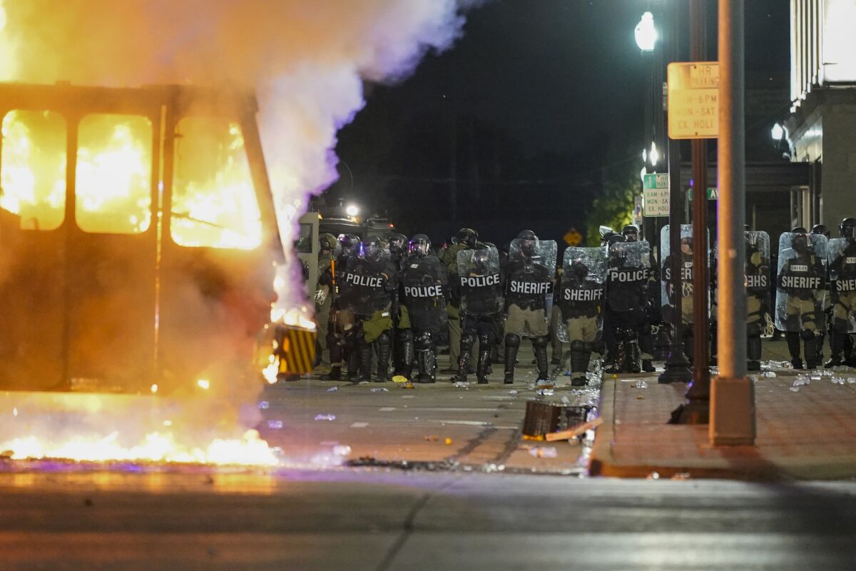 FILE - In this Aug. 24, 2020 file photo, police stand near a garbage truck ablaze during protests over the shooting of Jacob Blake in Kenosha, Wis. In the span of 48 hours, two Black men in U.S. cities hundreds of miles apart were shot by police in episodes that set off a national conversation about the need for officers to open fire on people walking away from them. (AP Photo/Morry Gash, File)