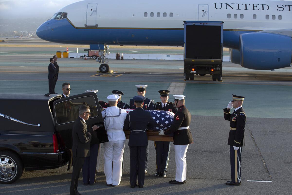 Service members in uniform load a flag-draped casket into a limousine
