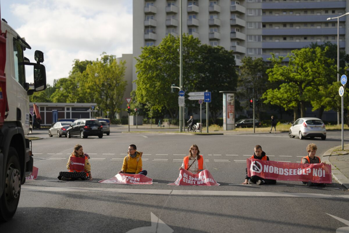 Climate activist Lina Schinkoethe, left, and her mother Solvig Schinkoethe, second from left, sit with their hands glued to the ground during a protest with the group Uprising of the Last Generation in Berlin, Germany, Tuesday, June 21, 2022. The group claims the world has only a few years left to turn the wheel around and avoid catastrophic levels of global warming. (AP Photo/Markus Schreiber)