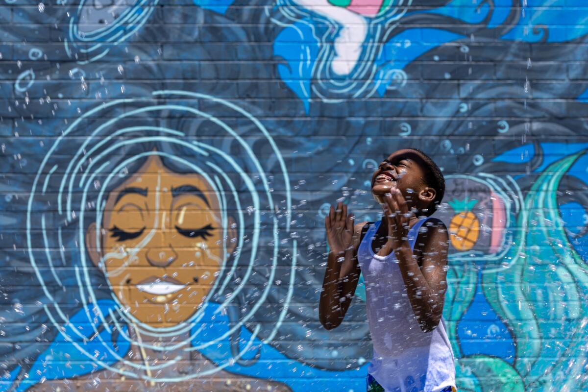 Water drops spray a smiling child in a tank top in front of a mural of a mermaid, her long, black hair floating in a blue sea