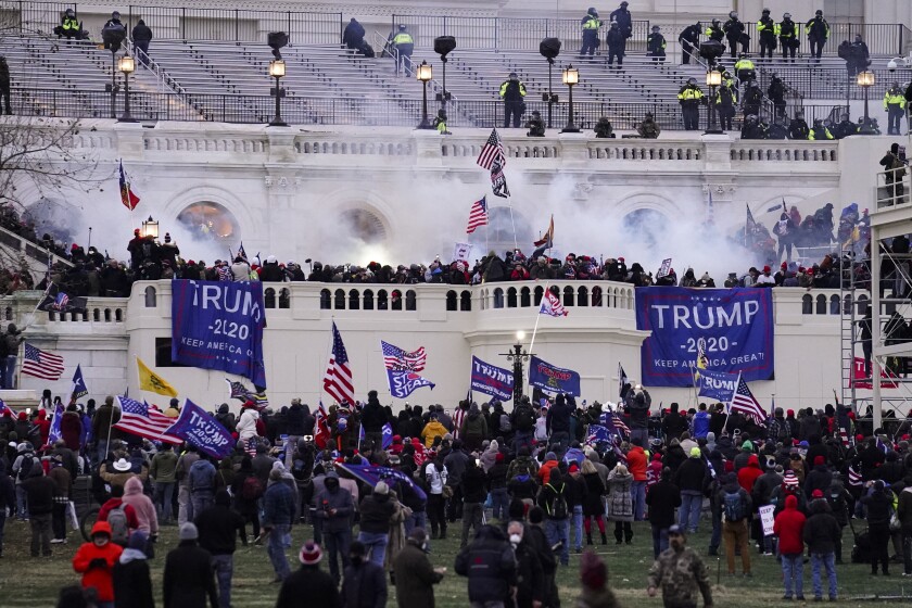 Clouds of tear gas smoke hover over a mob as it storms the U.S. Capitol waving blue "Trump 2020" banners.