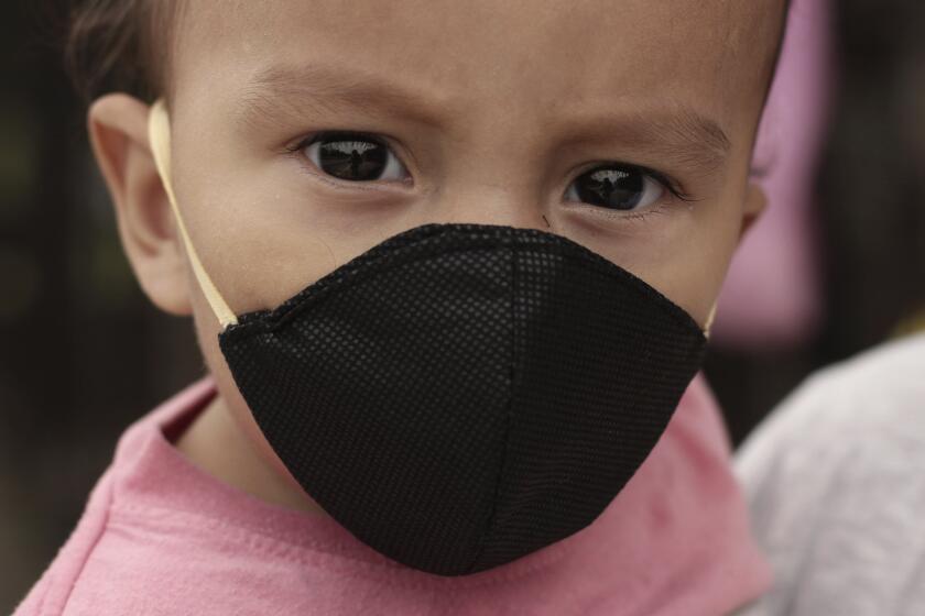 Gael Gómez, de un año, usa una mascarilla para protegerse del nuevo coronavirus mientras su madre lo sostiene para pedir comida en la Carretera de Oro en Ilopango, El Salvador, el martes 19 de mayo de 2020. (AP Foto/Salvador Melendez)