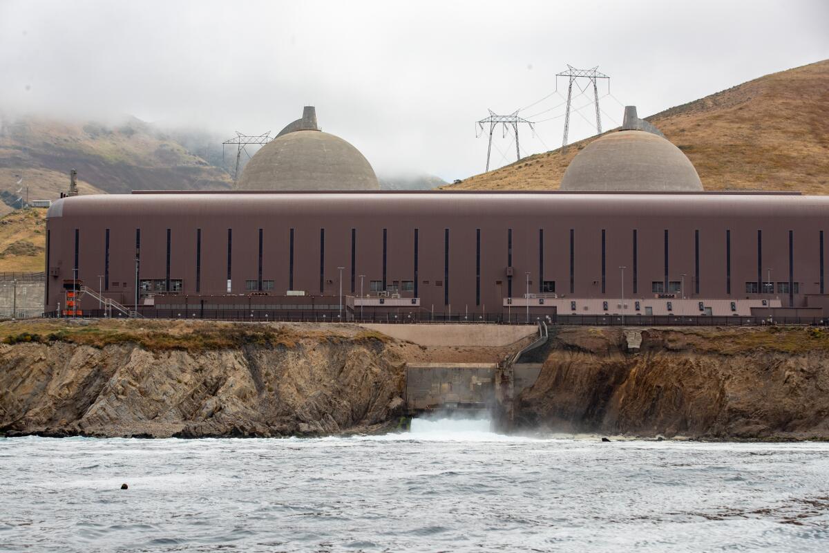 The Diablo Canyon containment domes on a foggy day, pictured from the water with power lines in the background.