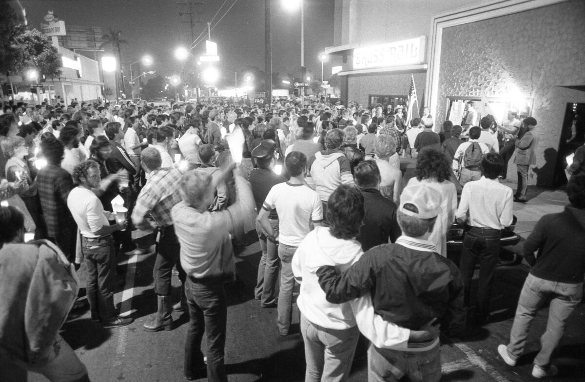 Black-and-white photo of a crowd of people, mostly men, gathered in the street, many of them holding candles