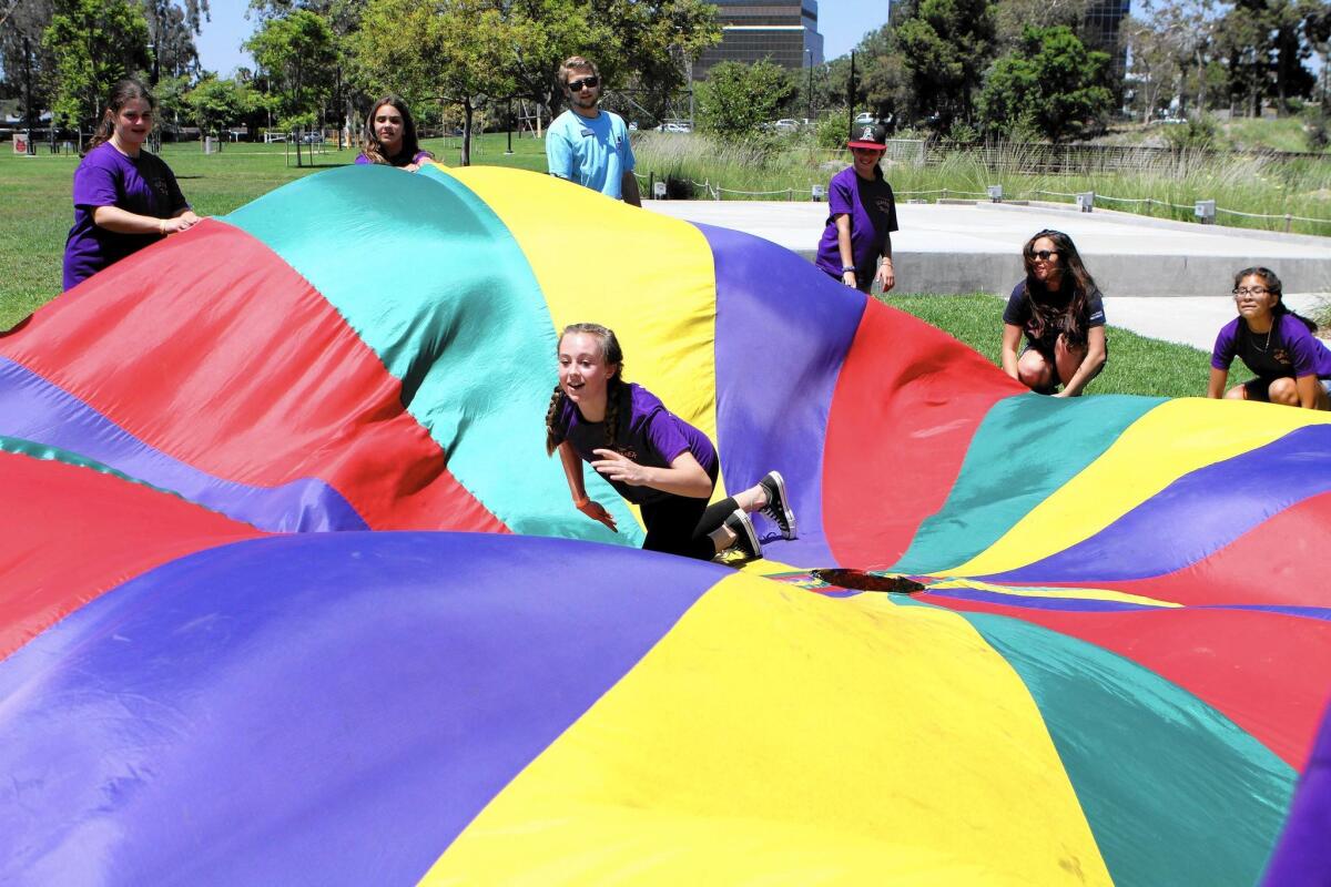 Olivia Galutza, 13, of Burbank plays the cat in a cat-and-mouse game with a large parachute at the annual Summer Daze Plus Teen Camp at Johnny Carson Park in Burbank on Thursday.