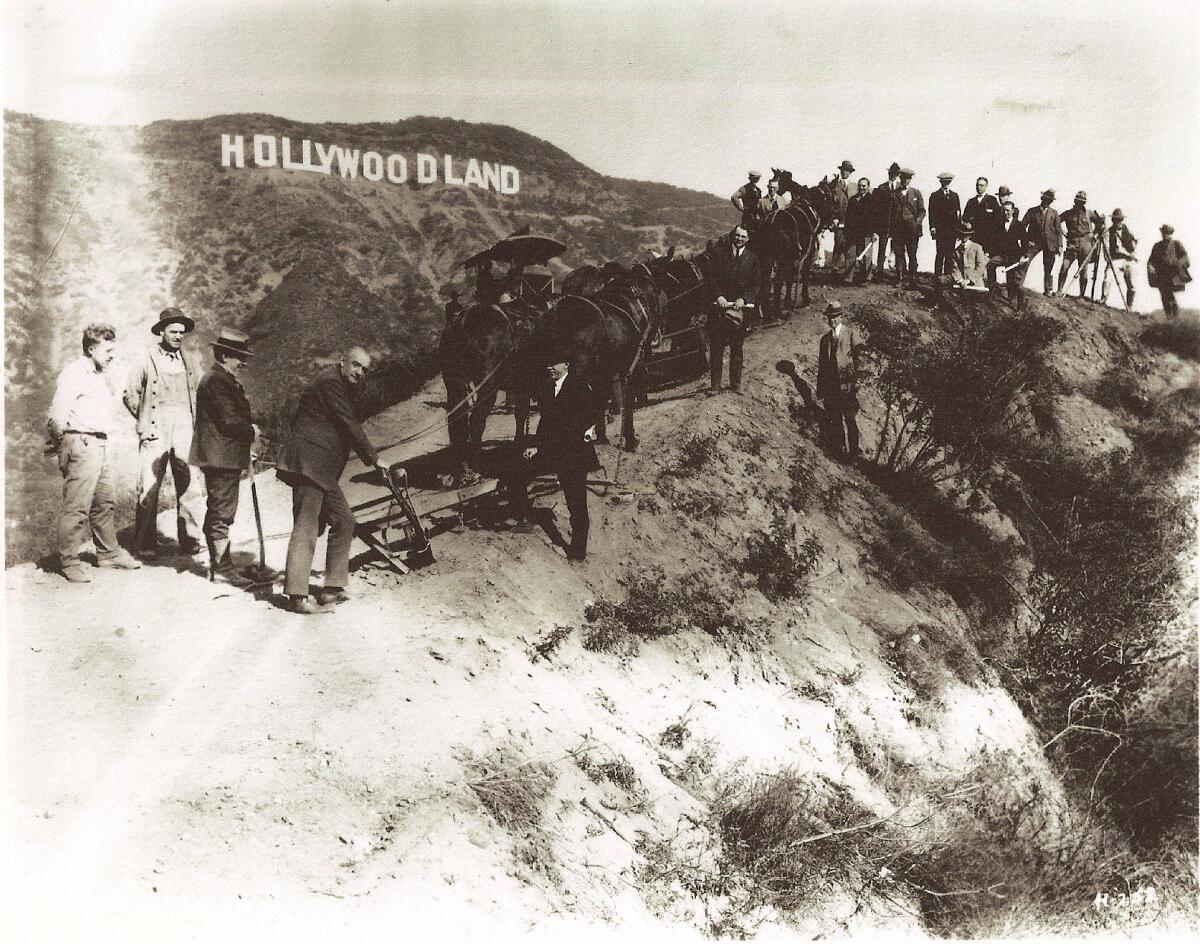 A 1923 photo of people standing along a ridge below the Hollywoodland sign.
